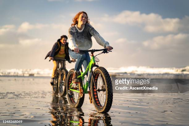 het jonge paar berijdt vette fietsen op het strand, getijdeflat - fat guy on beach stockfoto's en -beelden