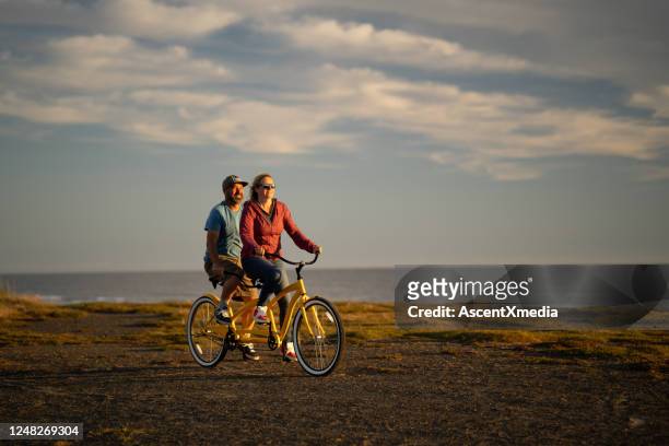 若いカップルは日の出にタンデムバイクに乗る - tandem ストックフォトと画像