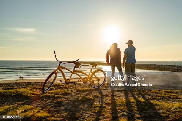 young couple relax on the beach at sunrise - tandem bicycle stock pictures, royalty-free photos & images