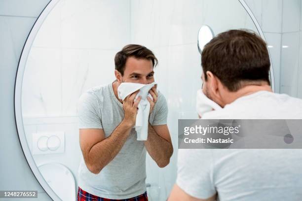 lächelnder junger mann waschen gesicht am morgen im badezimmer - man shaving face stock-fotos und bilder