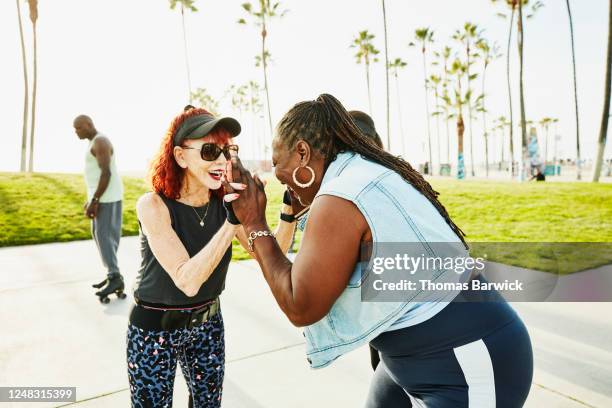 smiling senior women high fiving while roller skating in park - hoop earring 個照片及圖片檔