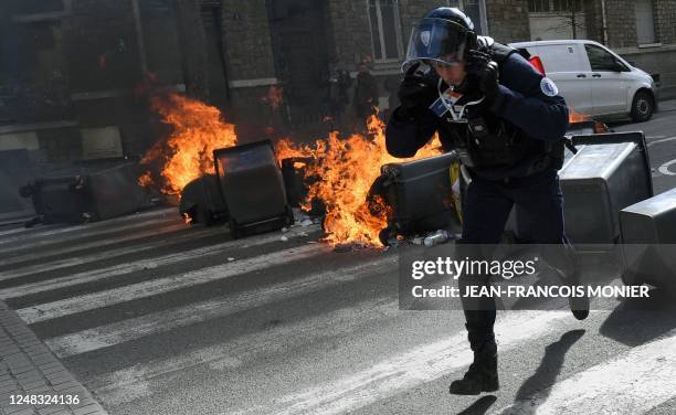 French policeman runs from burning rubbish bins laid across a street during a demonstration on the eighth day of strikes and protests across the...