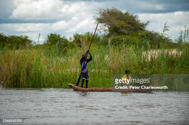 Man paddling his way along the Zambezi River with a woman in a dug out canoe . The river here delineates the border between Namibia and Zambia.