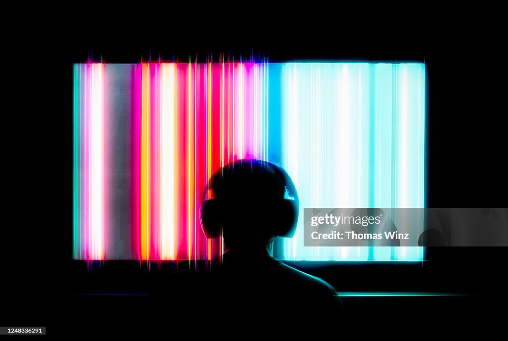 Silhouetted person with headphones watching large tv screen