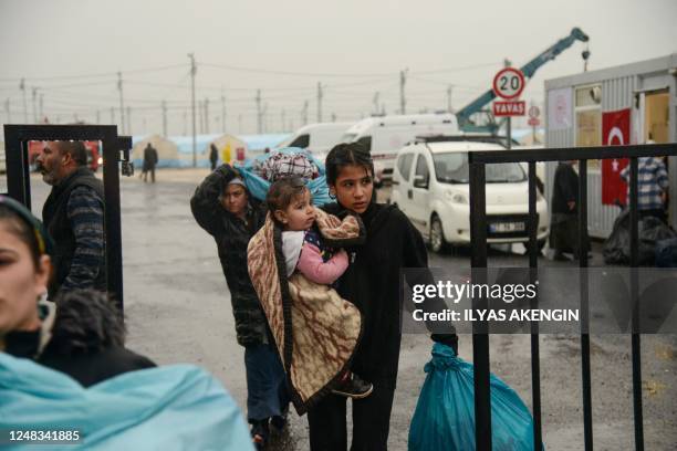 Women carry their belongings and a child as they leave a camp for those displaced after the February 6 earthquake, during heavy rains in Diyarbakir,...