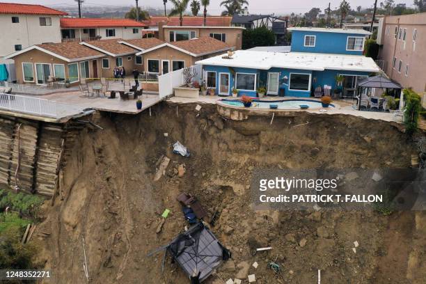 People look at a swimming pool sitting on the edge of a landslide below an apartment building following heavy rains from a winter storm in San...