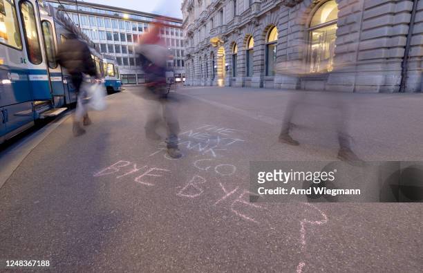 Long exposure shows people walking past a slogan written on the sidewalk in front of the global headquarters of Swiss bank Credit Suisse the day...