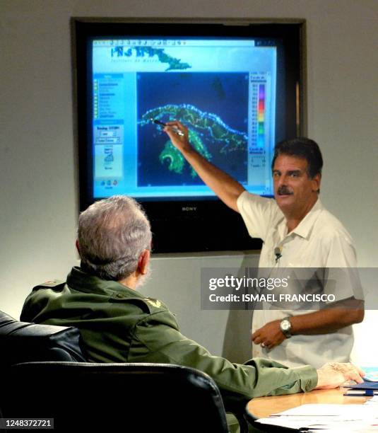 Cuban President Fidel Castro listens to the explanations given on an electronic display by the Cuban Metereological Intitute Chief Jose Rubiera on...