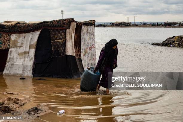 Woman pulls away a barrel from her tent submerged in floodwater inside the Sahlat al-Banat camp for internally displaced people, in the countryside...