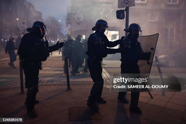 French police officers in riot gear operate in a tear gas cloud during a demonstration after the French government pushed a pensions reform through...