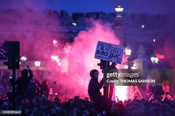 Protester on a traffic light holds a placard reading "Macron at the service of Black Rock, Black bloc at the service of the people" during a...