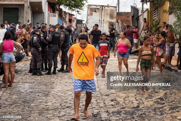 Police officers stand guard as people observe a burnt commercial truck in Natal, Rio Grande do Norte state, Brazil on 16 March 2023. - Gang members...