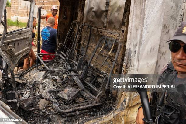 Policeman stands guard next to a burnt commercial truck in Natal, Rio Grande do Norte state, Brazil on 16 March 2023. - Gang members torched cars,...