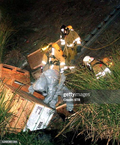 Firemen protected with special suits remove containers from a a shipment containing cyanide, that was transported by a truck that crashed on a bridge...