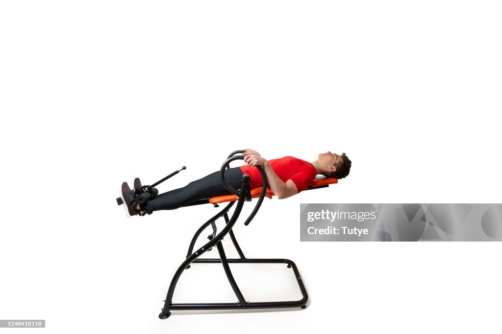 Man doing exercise on inversion table for his back pain, isolated on white