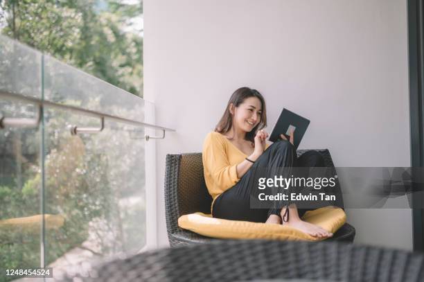 an asian chinese beautiful woman surf the net with her digital tablet in the afternoon at her balcony - choosing stock pictures, royalty-free photos & images