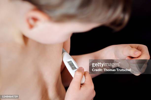 Symbolic photo on the subject of fever in small children. A five-year-old boy measures his body temperature with a clinical thermometer under his...