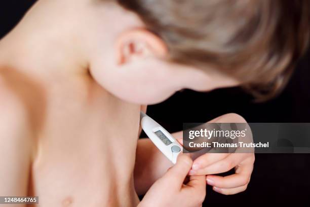 Symbolic photo on the subject of fever in small children. A five-year-old boy measures his body temperature with a clinical thermometer under his...