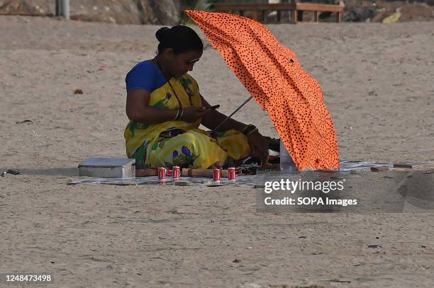 Woman shelters herself with an umbrella from the harsh sun as she checks her mobile phone in Mumbai. The city has been reeling under a heat wave in...