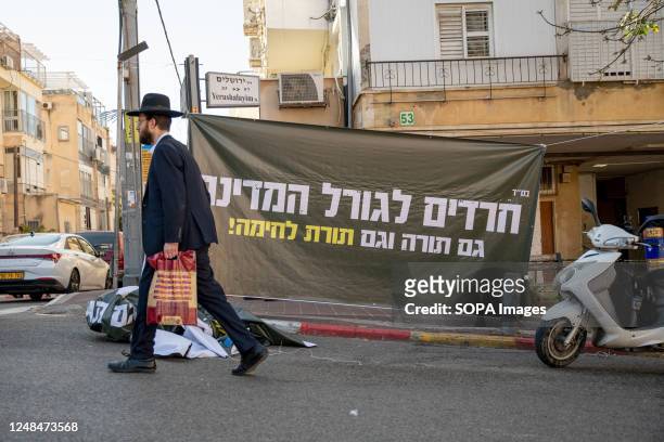 An orthodox man passes next to a protest against the reform banner that says 'Haredim/anxious for the fate of the country, Torah as well as martial...