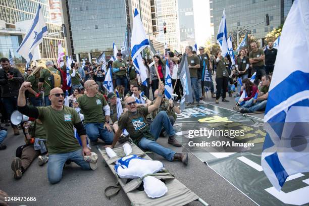 Israeli reserve soldiers against the judicial overhaul chant slogans in front of a stretcher with a figure and an Israeli flag during the...