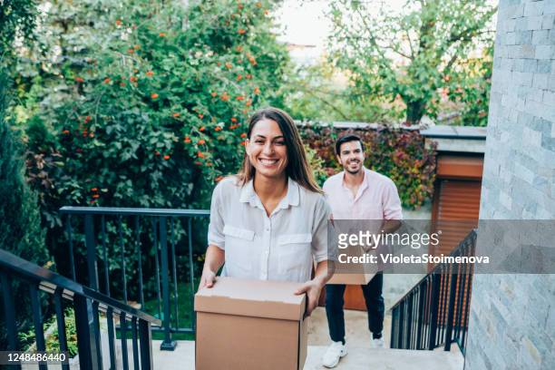 smiling couple carrying boxes into their new house. - entering stock pictures, royalty-free photos & images