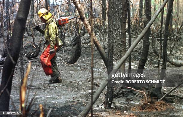 Clint Fuhrer, a firefighter with the South Dakota strike team, walks with a chain saw over his shoulder as his group works in putting out hot spots...