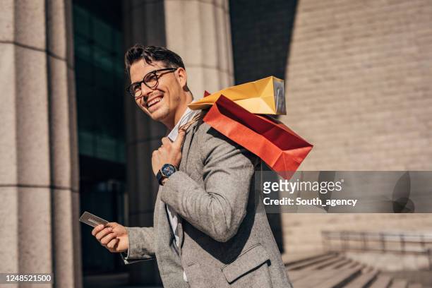ein hübscher mann shopaholic zu fuß in der stadt - shopping paper bag stock-fotos und bilder