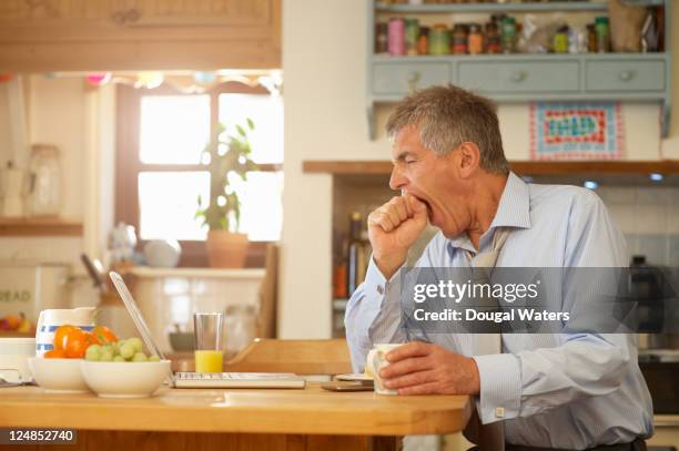 man yawning at kitchen table with laptop. - yawning stock pictures, royalty-free photos & images
