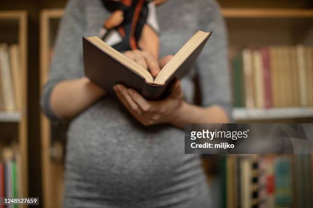 bella giovane donna incinta che tiene libro in biblioteca - studentessa di scuola secondaria foto e immagini stock