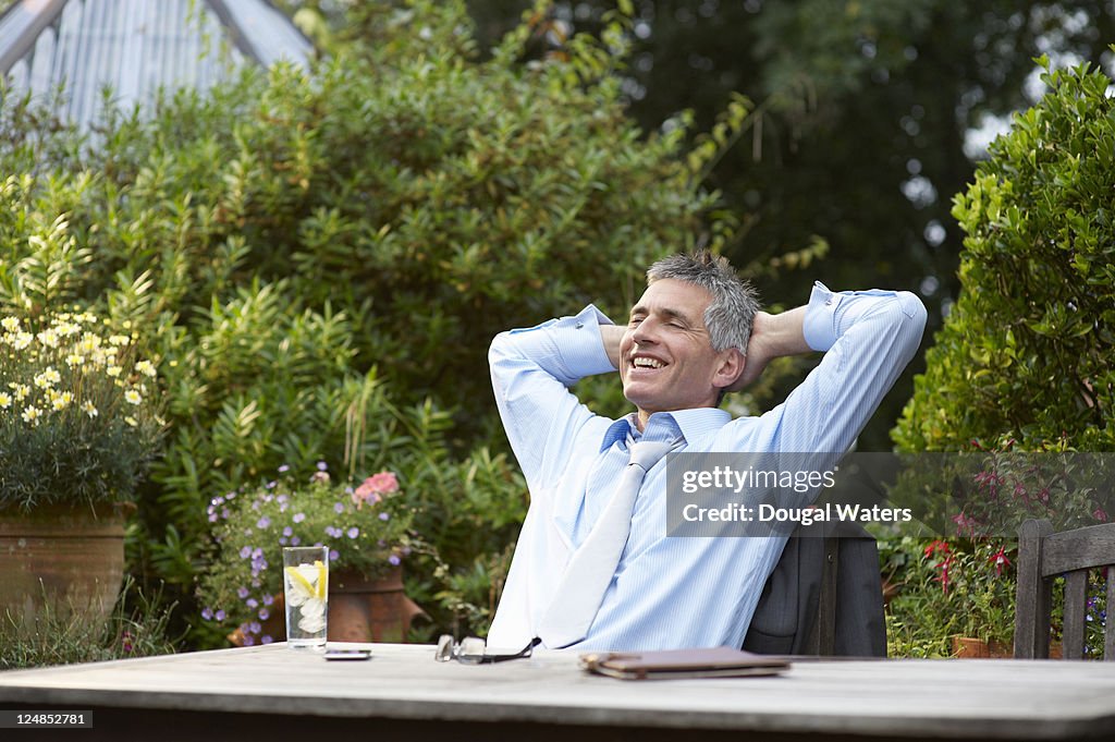 Man at garden table with hands behind head.