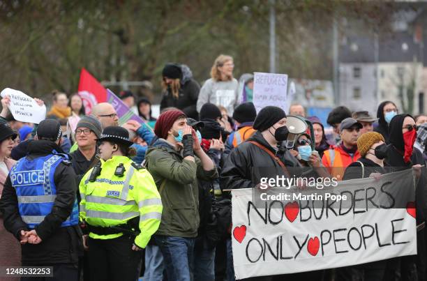 Protesters in support of refugees shout their message and hold a banner saying No Borders Only People outside the Novotel on March 18, 2023 in...