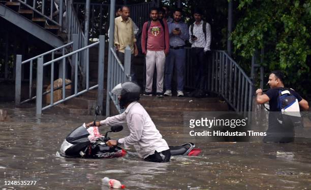 Commuter's two-wheeler stuck on the water-logged service lane amid heavy rain, at National Highway-48 near Narsinghpur village, on March 18, 2023 in...