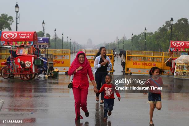 People protect themselves against rain at India Gate, after sudden change of weather from morning, on March 18, 2023 in New Delhi, India.