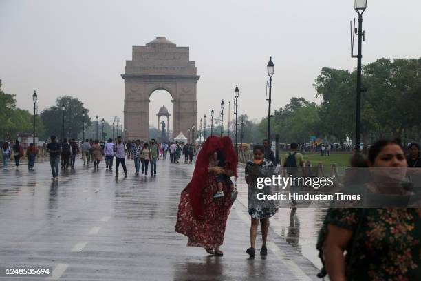 People protect themselves against rain at India Gate, after sudden change of weather from morning, on March 18, 2023 in New Delhi, India.