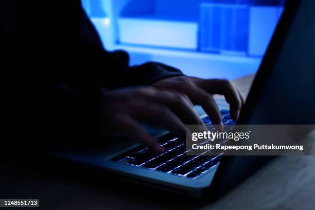 a computer programmer or hacker prints a code on a laptop keyboard to break into a secret organization system. internet crime concept. - computer hacker stock pictures, royalty-free photos & images