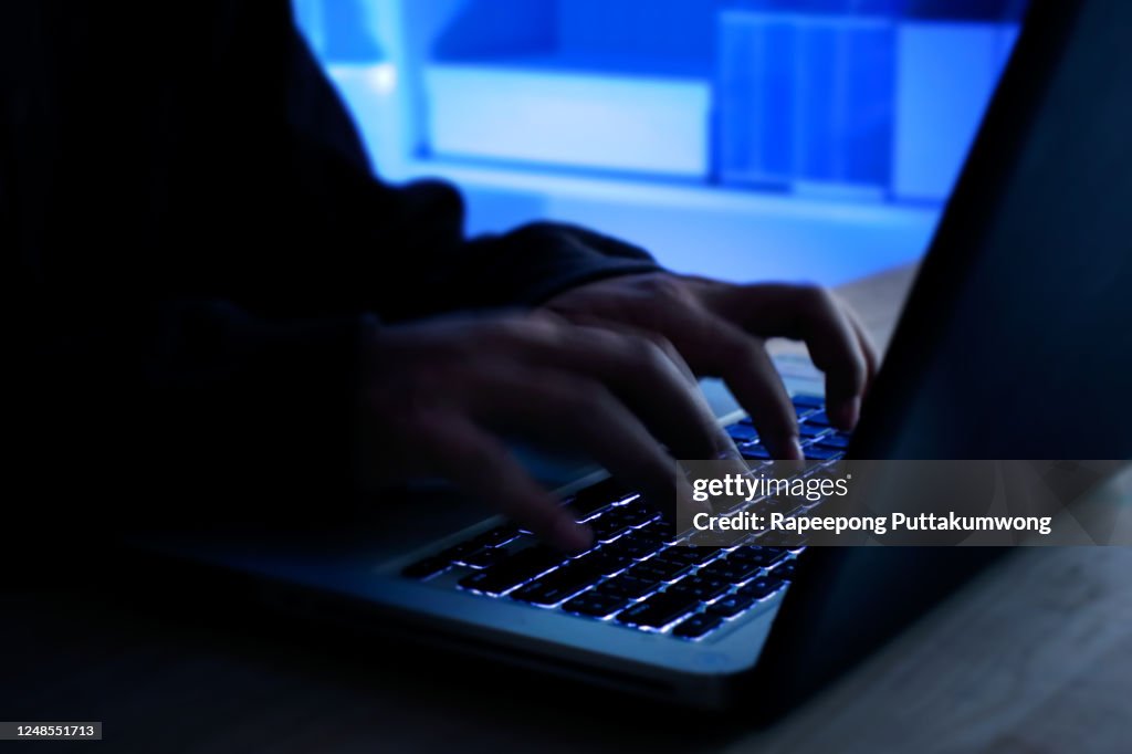 A computer programmer or hacker prints a code on a laptop keyboard to break into a secret organization system. Internet crime concept.