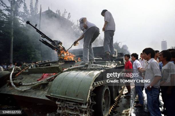 Chinese residents check a burning armoured personnel carrier which was put in on fire by rioters fighting back when the army opened fire on the...