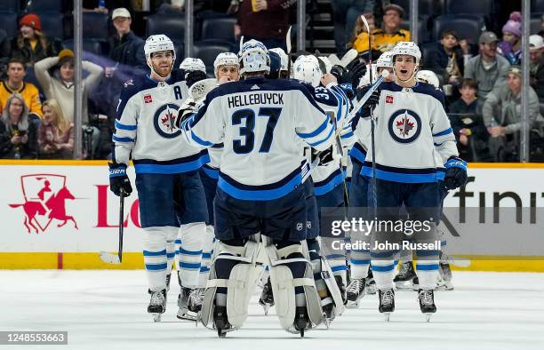 Adam Lowry and Morgan Barron congratulate Connor Hellebuyck of the Winnipeg Jets on a 3-2 win against the Nashville Predators during an NHL game at...