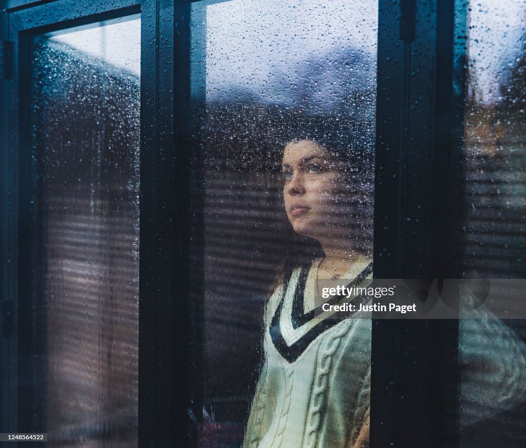 Teenage girl looking through wet window