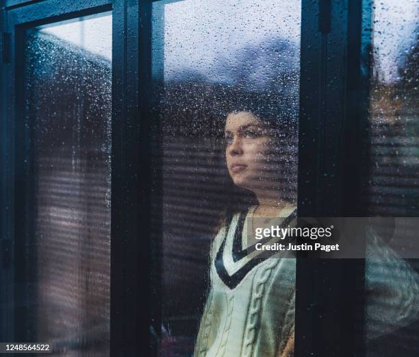 teenage girl looking through wet window - person looking through window stock pictures, royalty-free photos & images