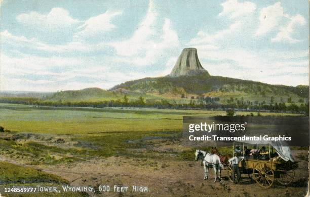Tinted postcard features a horse-drawn wagon at the fore and the Devil's Tower rock formation in the distance, eastern Wyoming, circa 1910.