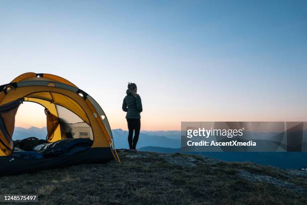 de jonge vrouw let op zonsopgang buiten het kamperen tent - wandelen buitensport stockfoto's en -beelden