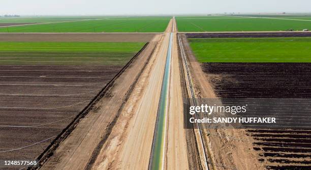 This aerial view shows an irrigation canal through agriculture fields in Holtville, California, on February 9, 2023. - A blanket of crops covers the...
