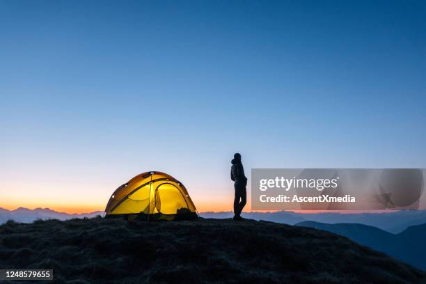 若い女性はキャンプテントの外で日の出を見ます - young woman standing against clear sky ストックフォトと画像