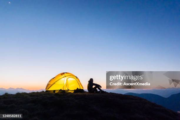 de jonge vrouw let op zonsopgang buiten het kamperen tent - sober leven stockfoto's en -beelden