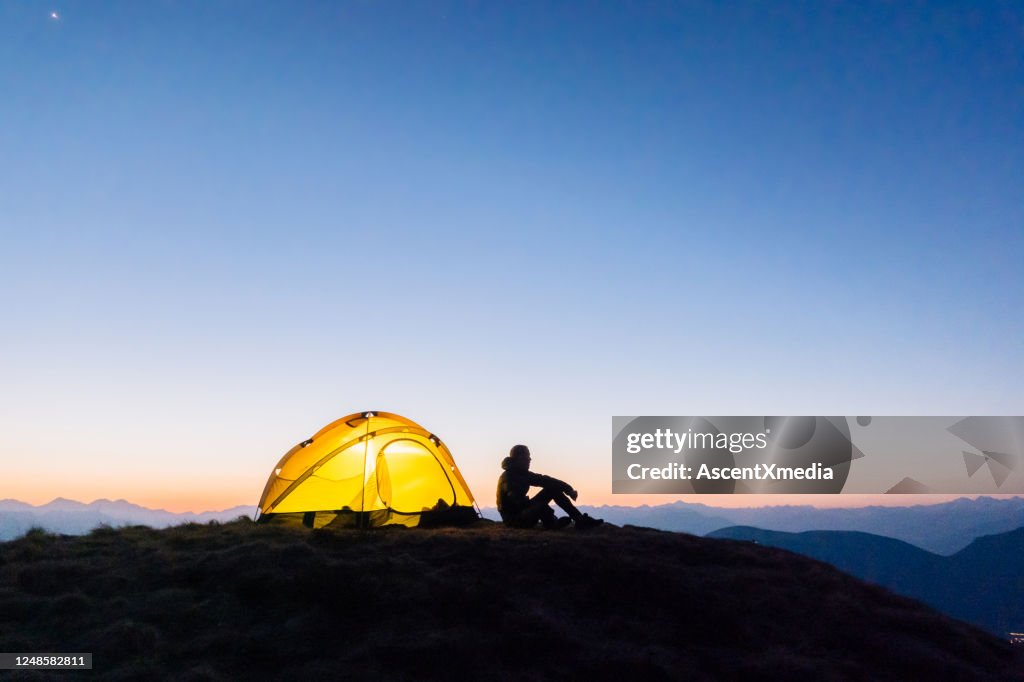 Young woman watches sunrise outside camping tent