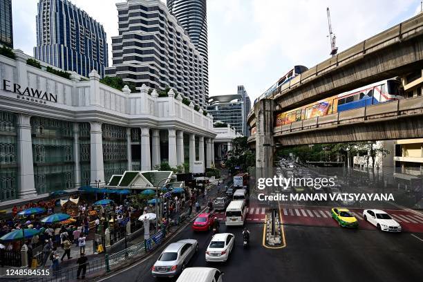 This photo taken on March 17, 2023 shows morning rush hour traffic and overhead BTS trains passing by as people offer prayers at the Erawan shrine in...