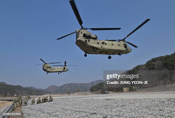 Soldiers take a position as US Army CH-47 Chinook helicopters prepare to land during a field artillery battalion gun raid drill at a military...