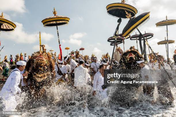 Balinese Hindus people carry sacred mask, sacred effigies and ritual paraphernalia during Melasti Ritual prior to Nyepi Day on March 19, 2023 at...